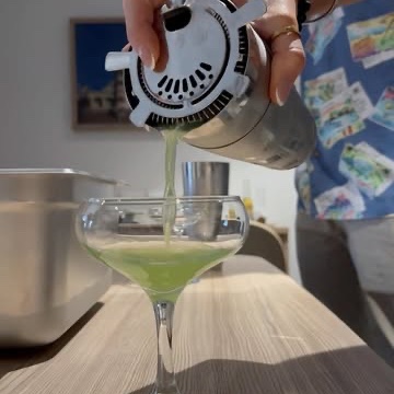 A green cocktail being strained on a timber bench